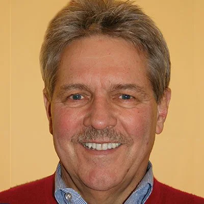 A man with gray hair and blue shirt smiling.